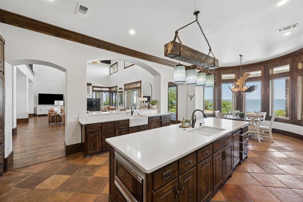 1180 McReynolds Road Sanger, TX 76266 - Photo 10 of 40 Spacious kitchen featuring a large central island with white countertop and integrated sink, rich wood cabinetry, and a beamed ceiling detail