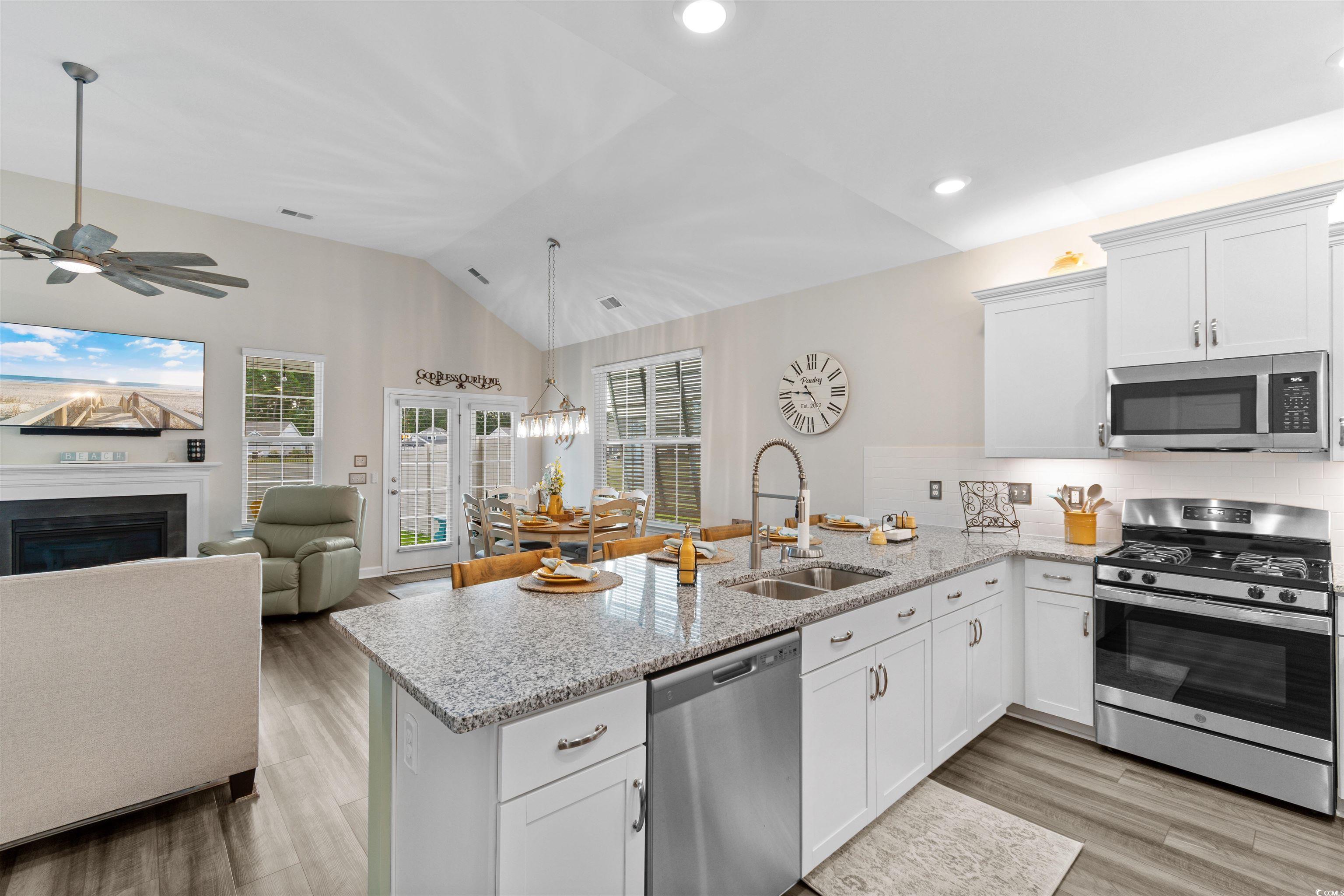 240 Sundew Loop Little River, SC 29566 - Photo 8 of 40 Kitchen with appliances with stainless steel finishes, a peninsula, lofted ceiling, a fireplace, and white cabinetry