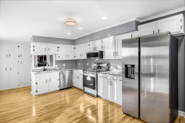 a kitchen with stainless steel appliances granite countertop a refrigerator a sink dishwasher a stove and white cabinets with wooden floor