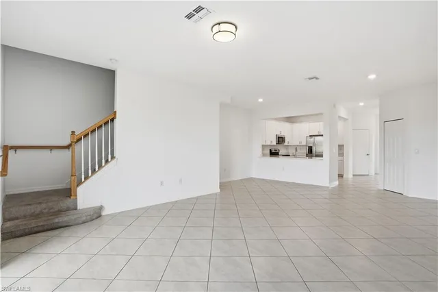 a view of an empty room and kitchen view with wooden floor