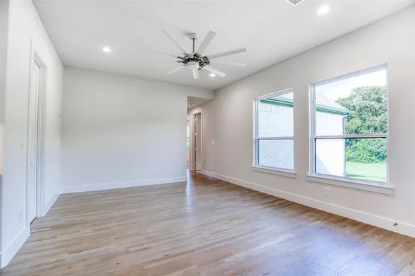 an empty room with wooden floor chandelier fan and windows