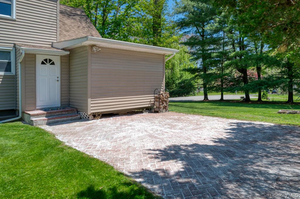 6 Winterberry Road Fishkill, NY 12524 - Photo 39 of 43 Paver patio featuring a side entry door with fanlight window, extending to a grassy yard with mature trees