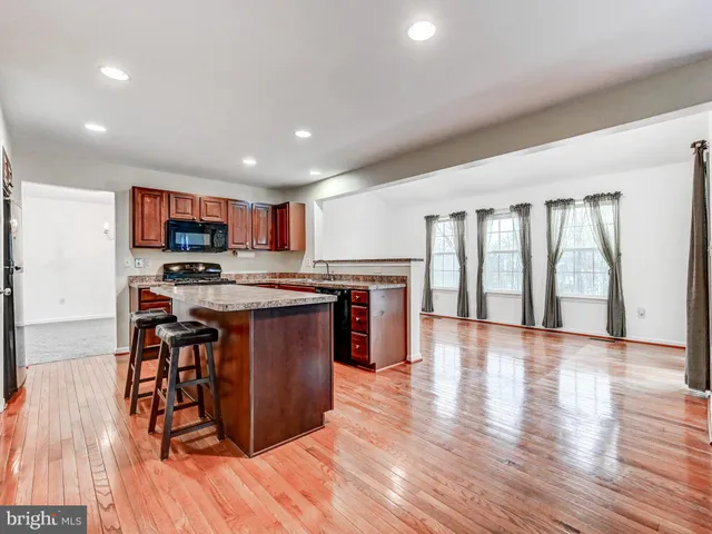 a open kitchen with stainless steel appliances granite countertop a stove top oven a dining table and chairs with wooden floor