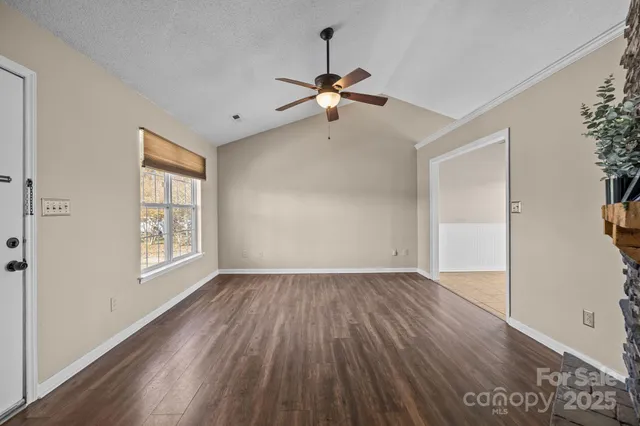 an empty room with wooden floor chandelier fan and windows