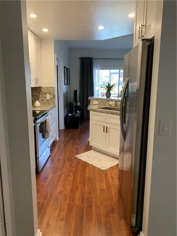 a kitchen with stainless steel appliances granite countertop a refrigerator a sink dishwasher a stove and white countertops with wooden floor