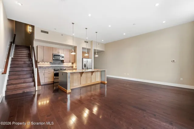 a kitchen with stainless steel appliances granite countertop a sink a oven a dining table and chairs with wooden floor