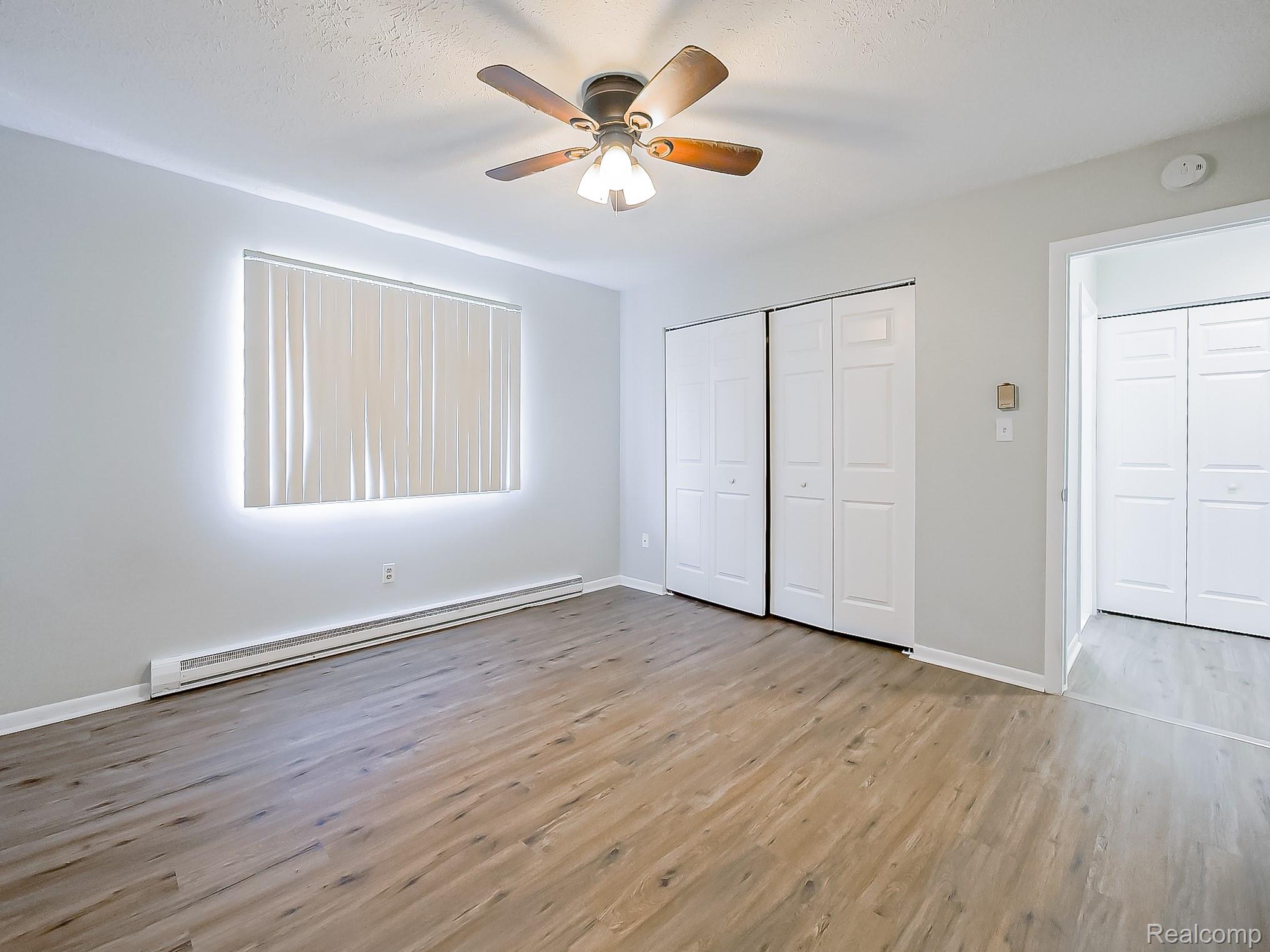 125 East Van Riper Road, Unit 7 Fowlerville, MI 48836 - Photo 13 of 26 Unfurnished bedroom featuring a baseboard heating unit, light wood-style floors, a ceiling fan, and a closet