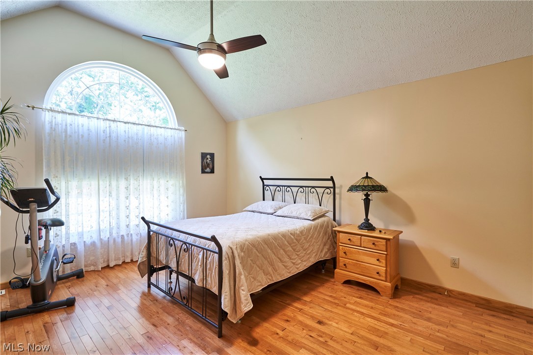 1963 Haines Road Madison, OH 44057 - Photo 11 of 34 Vaulted ceiling bedroom featuring a large arched window with transom, wood-finish flooring, and a ceiling fan with integrated lighting