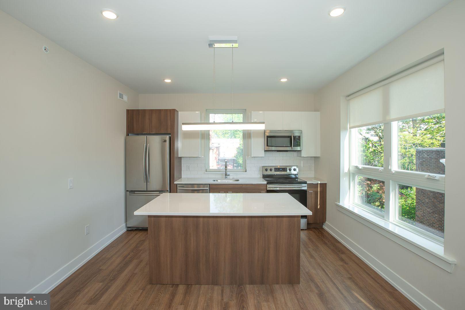 4534 Spruce Street, Unit 2BA2 Philadelphia, PA 19139 - Photo 4 of 9 a large kitchen with stainless steel appliances a large counter top a stove a chimney a sink and a large window