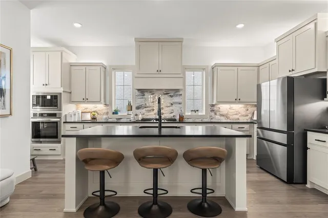 a kitchen with stainless steel appliances a sink a stove a refrigerator cabinets and chairs