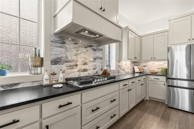 a kitchen with stainless steel appliances granite countertop a sink a refrigerator and white cabinets