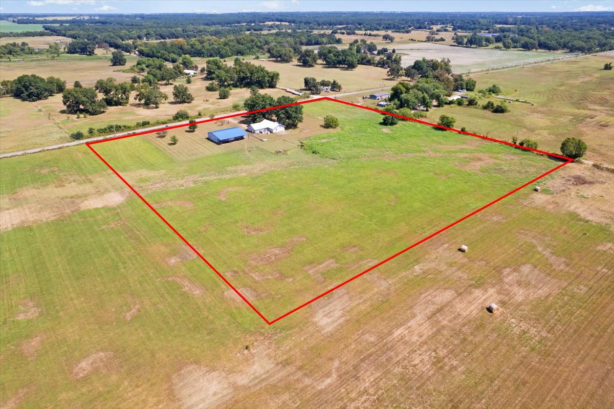 Expansive agricultural land featuring a primary residence, a large blue outbuilding, and scattered mature trees
