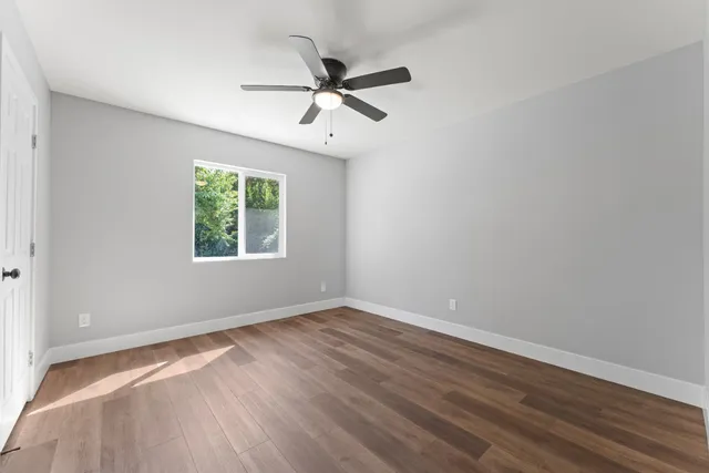 an empty room with wooden floor fan and windows