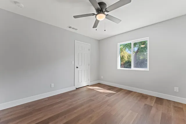 an empty room with wooden floor ceiling fan and windows