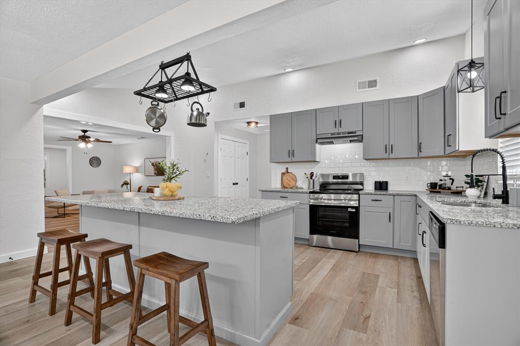 795 Meadow Road Springtown, TX 76082 - Photo 6 of 25 Kitchen featuring an island with a light-toned countertop, gray cabinetry, stainless steel appliances, wood-finish flooring, and a subway tile backsplash