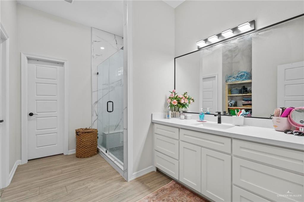 23247 Uresti Road Edinburg, TX 78542 - Photo 18 of 18 Spacious bathroom featuring a double vanity with ample cabinetry, a large frameless mirror, a walk-in shower with a built-in bench, and wood-finish flooring