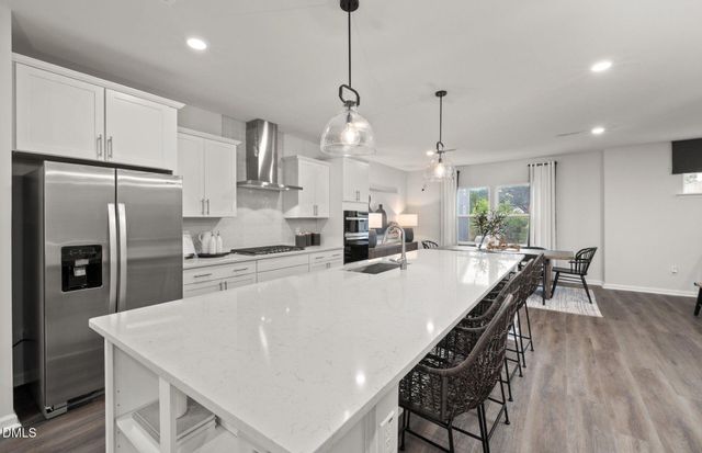 a kitchen with stainless steel appliances a stove a sink a dining table chairs and a refrigerator