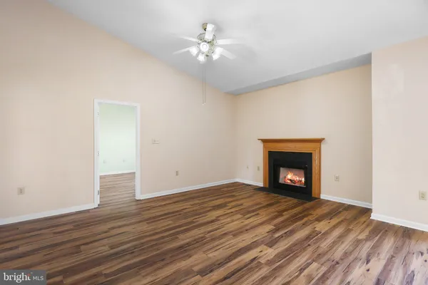 a view of an empty room with wooden floor a fireplace and a window