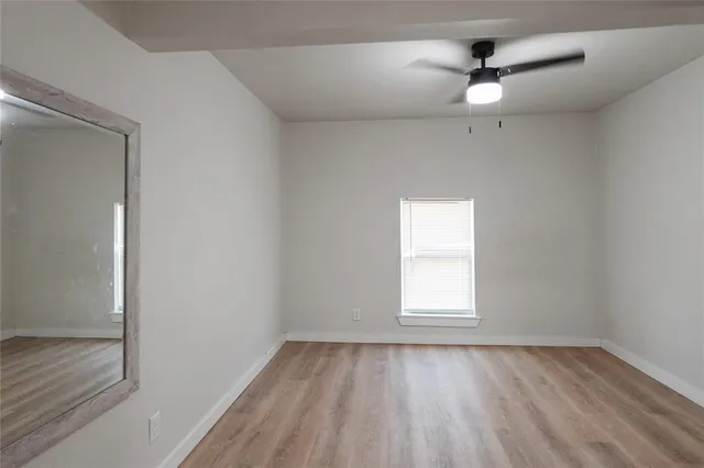 an empty room with wooden floor fan and windows