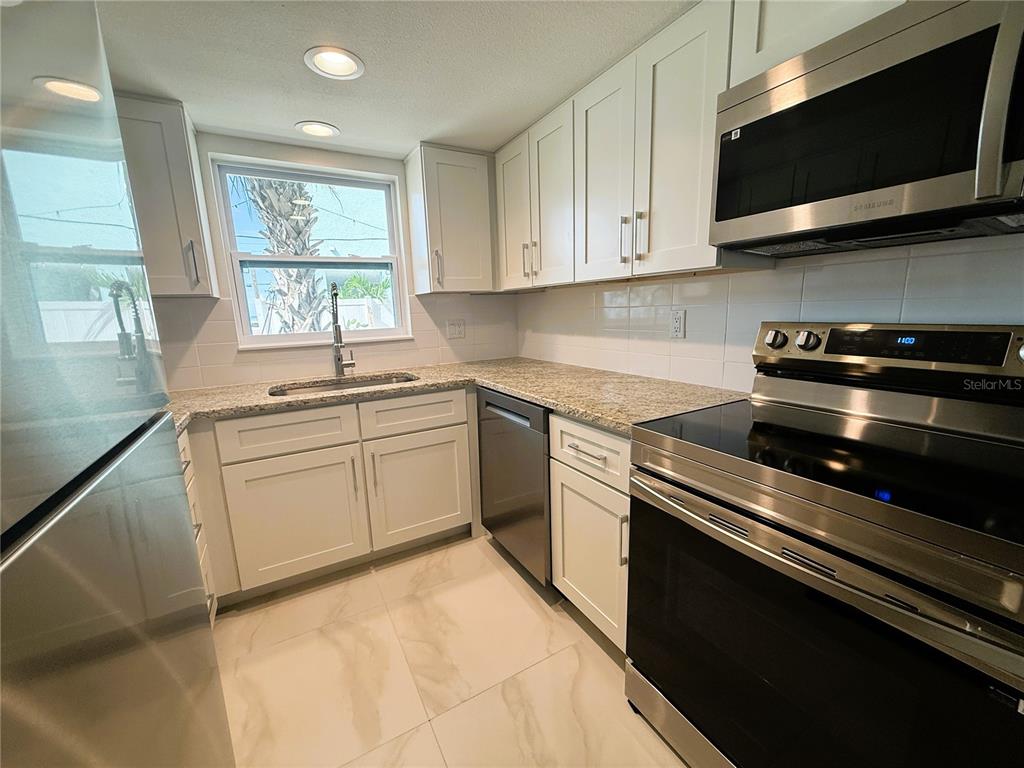 14120 Palm Street, Unit 104 Madeira Beach, FL 33708 - Photo 4 of 18 a kitchen with stainless steel appliances a sink dishwasher stove microwave and cabinets