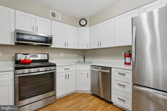 a kitchen with stainless steel appliances granite countertop a refrigerator a stove a dining table and chairs with wooden floor