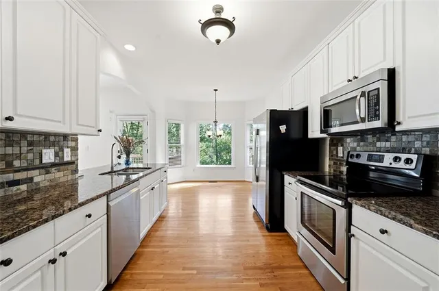 a kitchen with granite countertop a stove a sink dishwasher a refrigerator and cabinets with wooden floor