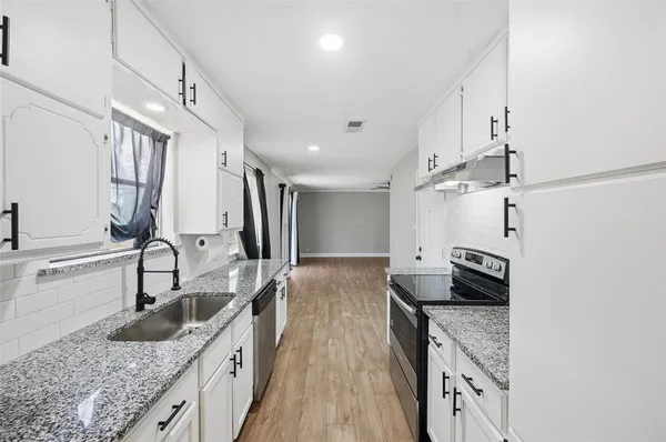 a kitchen with granite countertop a sink a counter top space stainless steel appliances and cabinets