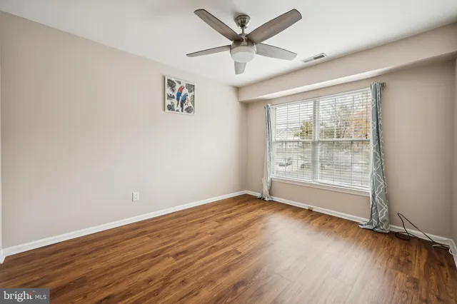 an empty room with wooden floor fan and windows
