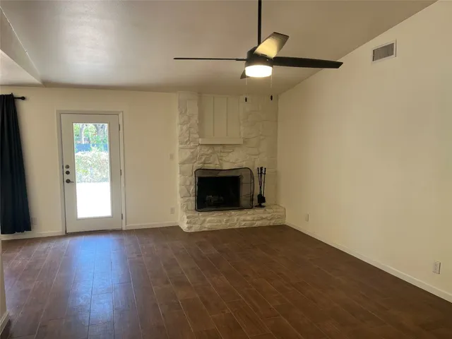 an empty room with wooden floor fireplace and windows
