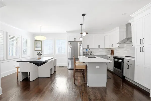 a kitchen with stainless steel appliances granite countertop a sink a stove a refrigerator and white cabinets with wooden floor