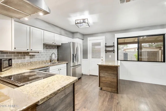 a kitchen with stainless steel appliances granite countertop a stove a refrigerator a sink and white cabinets with wooden floor