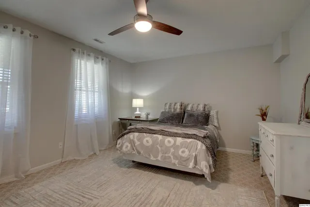 a spacious bedroom with a bed and a lamp on dresser