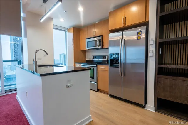 a kitchen with stainless steel appliances granite countertop a refrigerator a stove and a sink with wooden floor