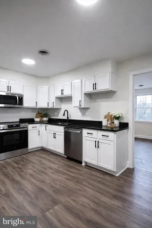 a kitchen with granite countertop wooden floors stainless steel appliances and white cabinets