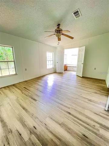 an empty room with wooden floor ceiling fan and windows