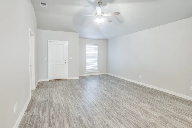 an empty room with wooden floor chandelier fan and windows