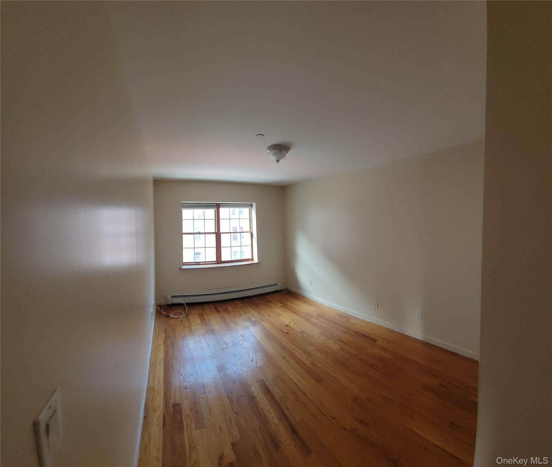 108-27 63rd Avenue, Unit 3B Queens, NY 11375 - Photo 13 of 17 an empty room with wooden floor and windows