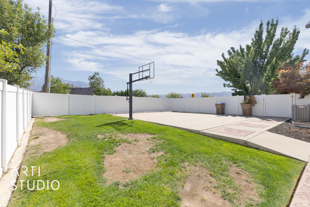 704 West Vahe Street Draper, UT 84020 - Photo 32 of 35 Expansive backyard featuring a concrete pad with a basketball hoop, a manicured lawn, and white privacy fencing