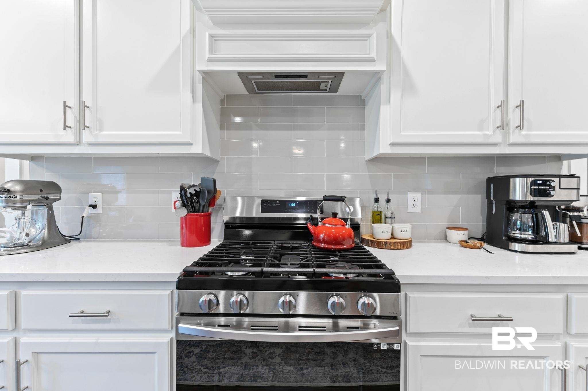 13233 Ibis Boulevard Daphne, AL 36527 - Photo 19 of 100 Modern kitchen featuring a stainless steel gas range, a coordinating range hood, white shaker-style cabinetry with brushed nickel hardware, light-colored countertops, and a gray subway tile backsplash