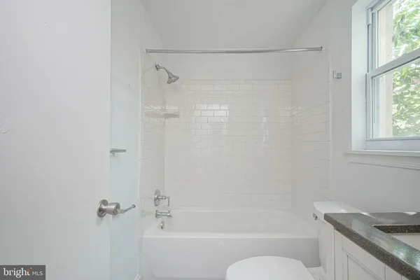 a bathroom with a granite countertop bathtub shower sink vanity and a toilet