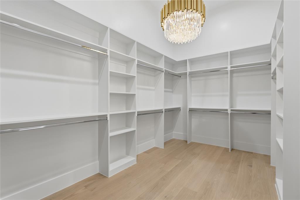 6038 Prospect Avenue Dallas, TX 75206 - Photo 21 of 40 Walk-in closet featuring built-in white shelving, chrome hanging rods, wood-finish flooring, and a gold-tone chandelier with crystal accents
