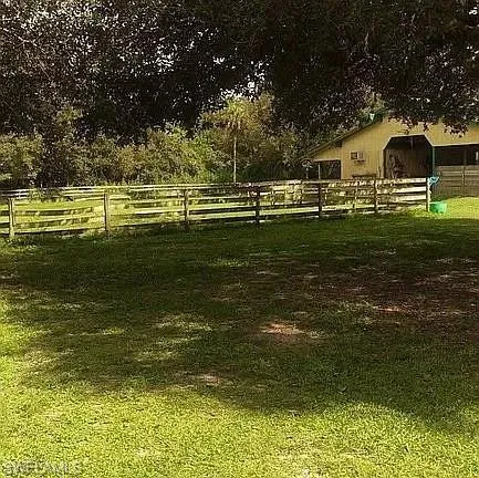 a view of a yard with wooden fence and large trees