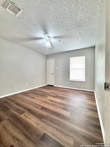 a view of empty room with wooden floor and fan