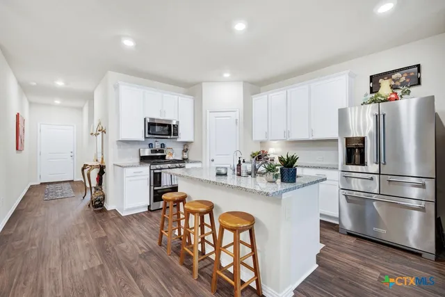 a kitchen with granite countertop a refrigerator oven a sink dishwasher and white cabinets with wooden floor