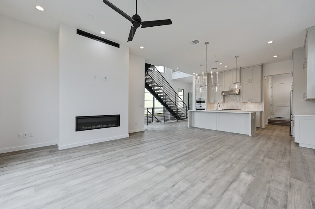 6805 Adeline Way, Unit 17 Austin, TX 78746 - Photo 14 of 38 Unfurnished living room with a glass covered fireplace, stairs, ceiling fan, recessed lighting, and light wood-style floors