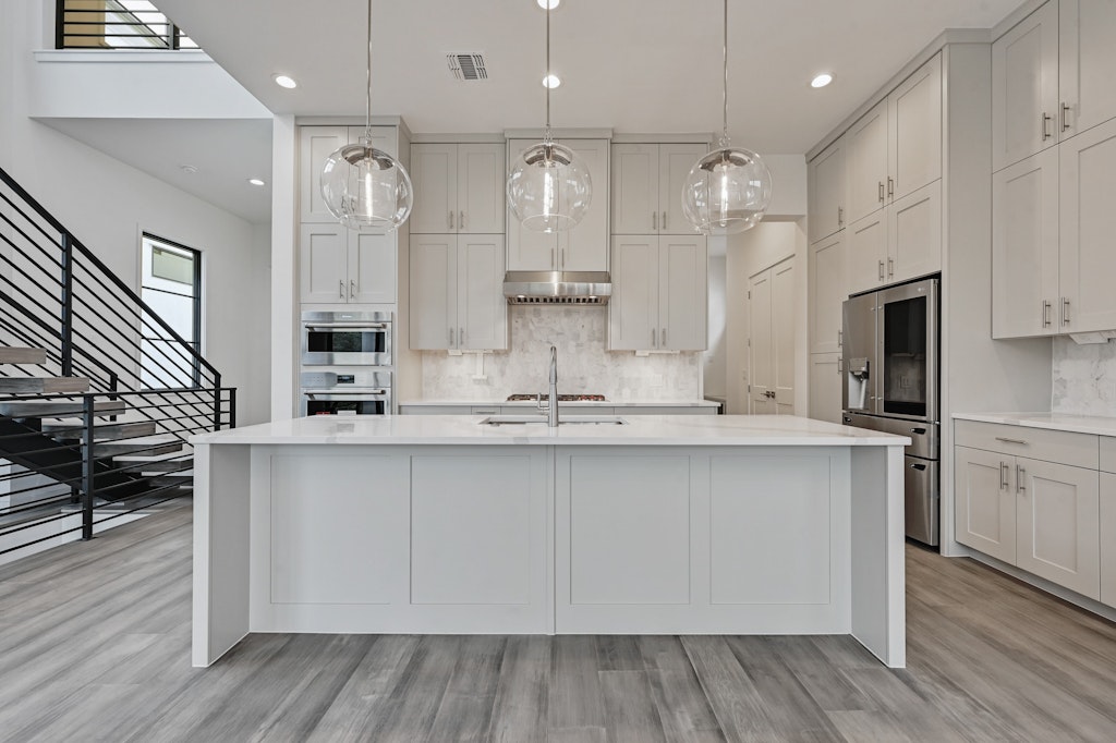 6805 Adeline Way, Unit 17 Austin, TX 78746 - Photo 10 of 38 Kitchen featuring light stone counters, hanging light fixtures, appliances with stainless steel finishes, light wood finished floors, and a large island with sink