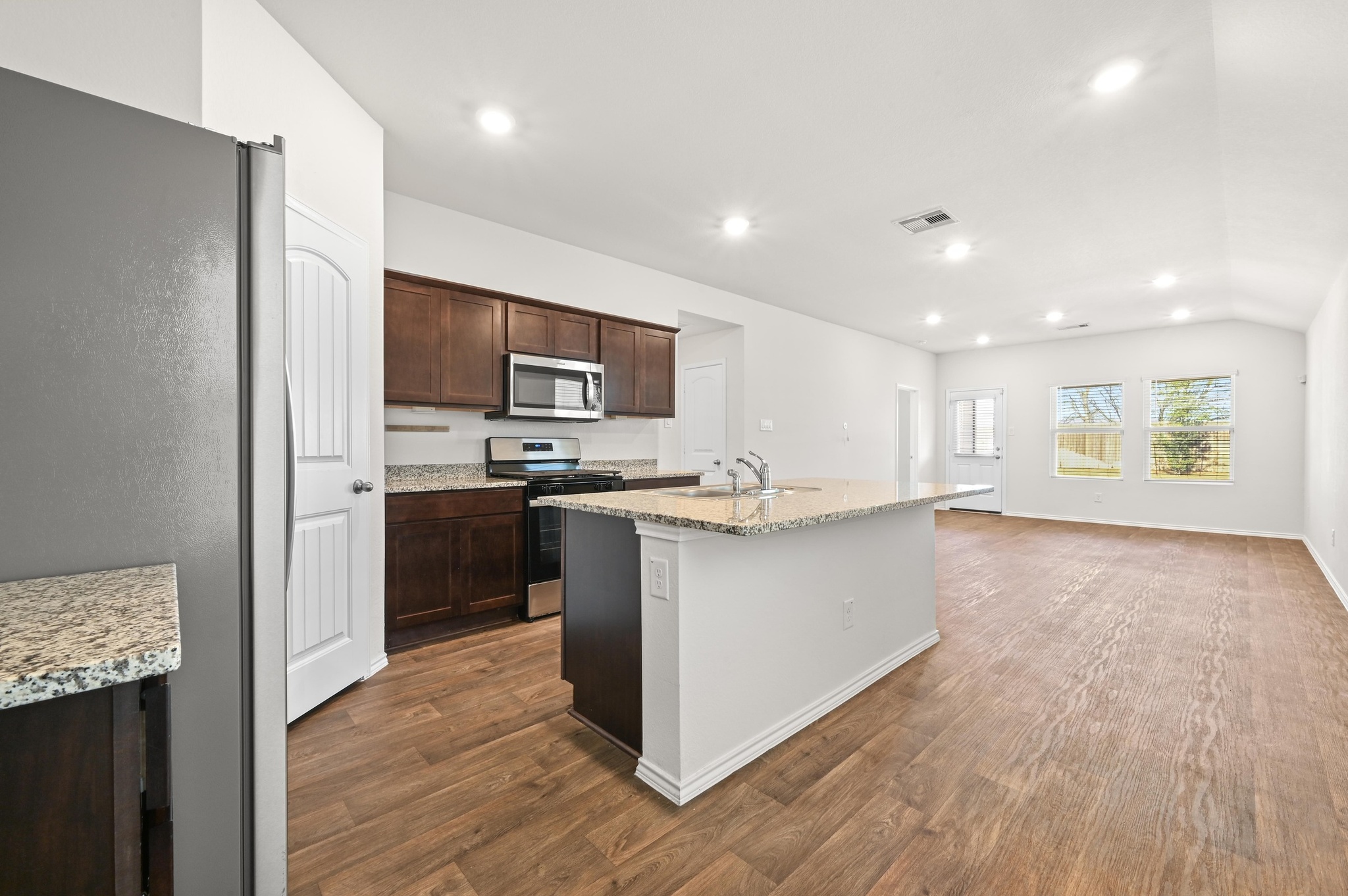412 Sickle Loop Kyle, TX 78640 - Photo 5 of 25 Kitchen featuring stainless steel appliances, an island with sink, light stone counters, dark wood-type flooring, and recessed lighting