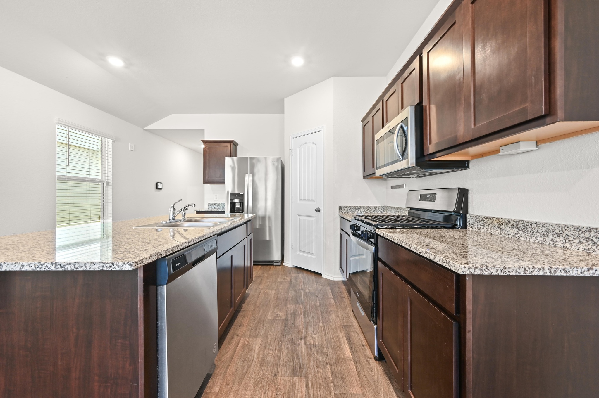 412 Sickle Loop Kyle, TX 78640 - Photo 7 of 25 Kitchen with stainless steel appliances, dark wood finish cabinetry, dark wood-style floors, light stone counters, and a kitchen island with sink
