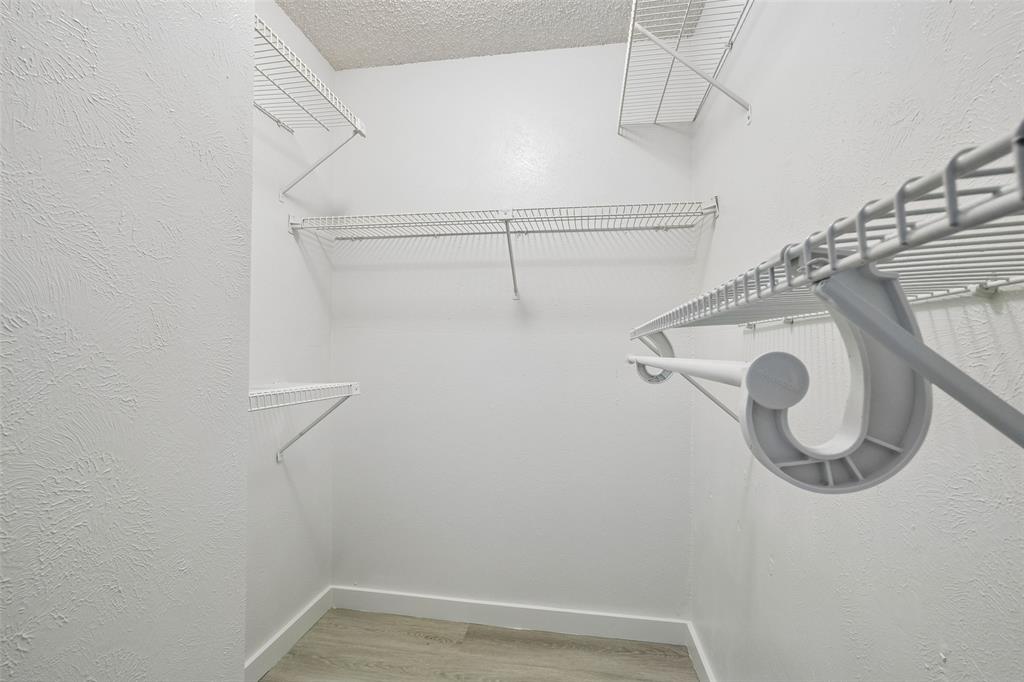 11480 Audelia Road, Unit 136 Dallas, TX 75243 - Photo 17 of 29 Walk-in closet for primary bedroom with multiple wire shelving units and hanging rods, white walls, and wood-finish flooring