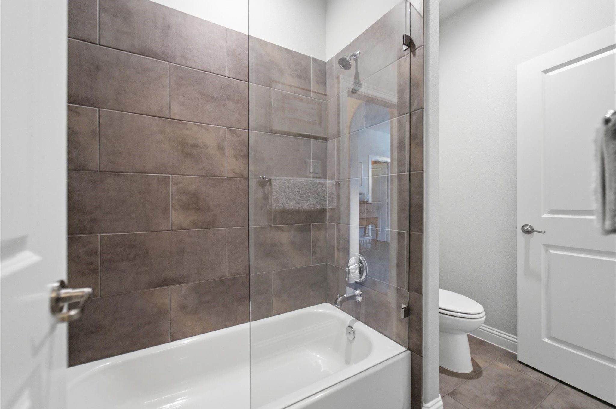 23722 Thortons Park Lane Spring, TX 77389 - Photo 38 of 48 This bathroom features a modern design with a tiled shower and tub combination, glass door, and neutral tones. The room is well-lit and includes a toilet and sleek fixtures.